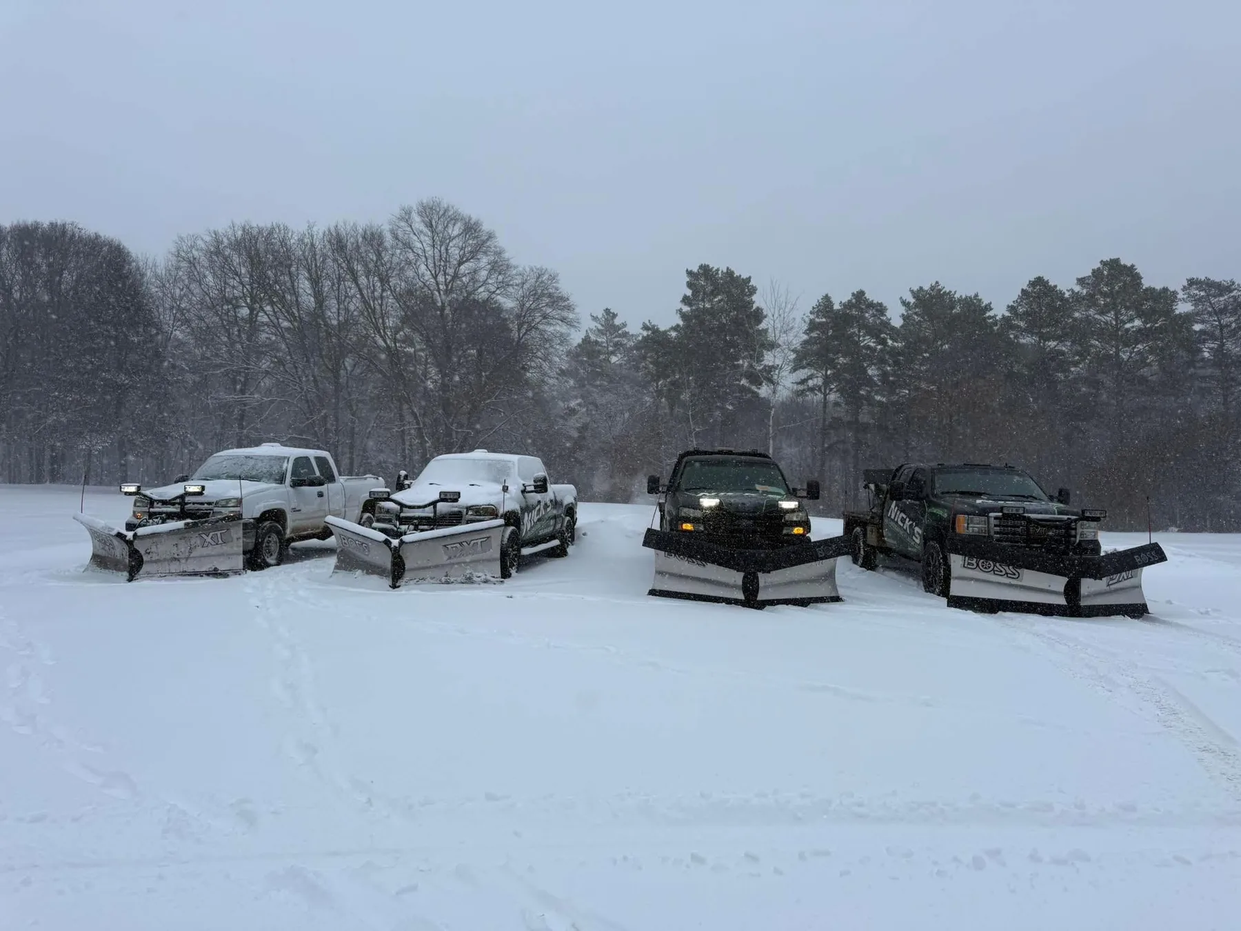 Several of Nick's snow plow trucks lined up on a snowy property
